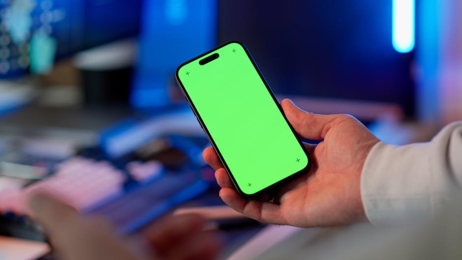 Hand holding a smartphone with a green screen in a modern indoor setting, ready for app design or mockup.