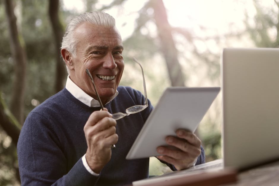 Elderly man using a tablet and laptop in a serene outdoor setting.