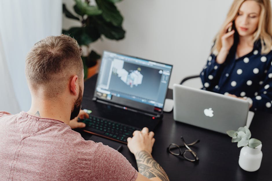 Two professionals working on laptops, engaging in a collaborative office environment.