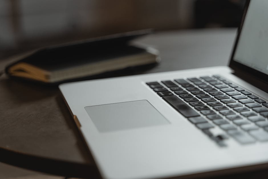 Close-up of a laptop keyboard on a desk with a notebook in soft focus.