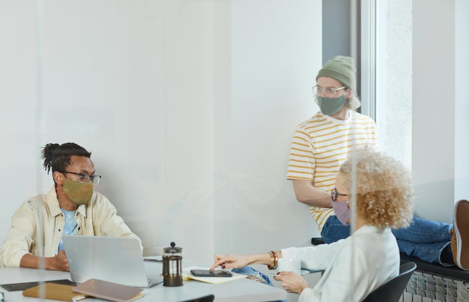 Colleagues engage in a team discussion while wearing face masks, highlighting pandemic office practices.