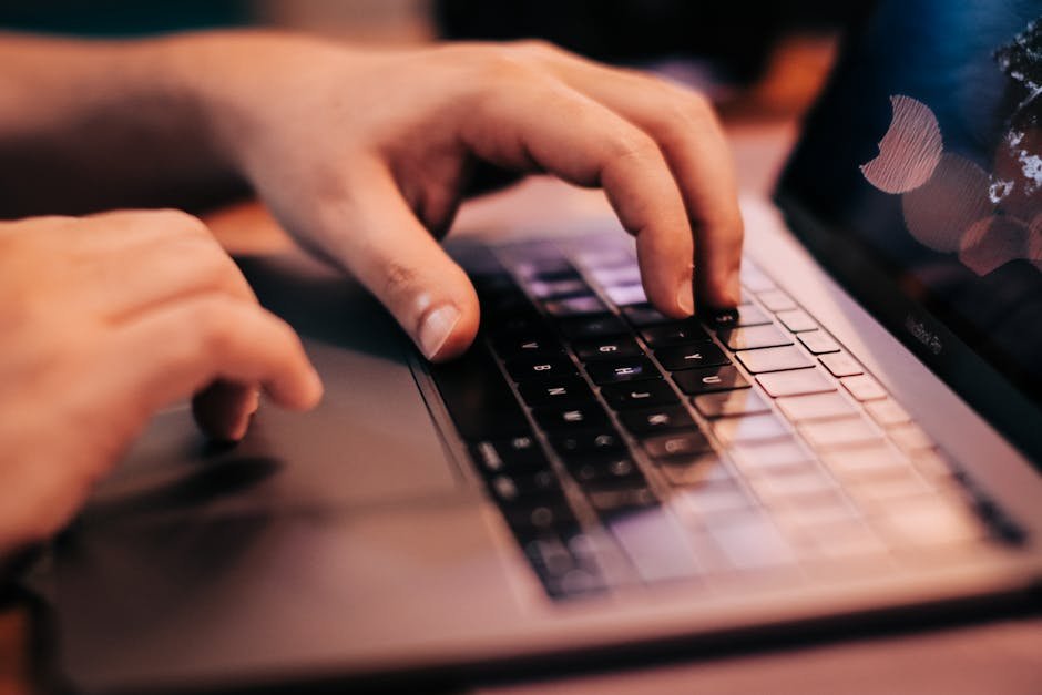 A person typing on a laptop with focus on hands and keyboard.