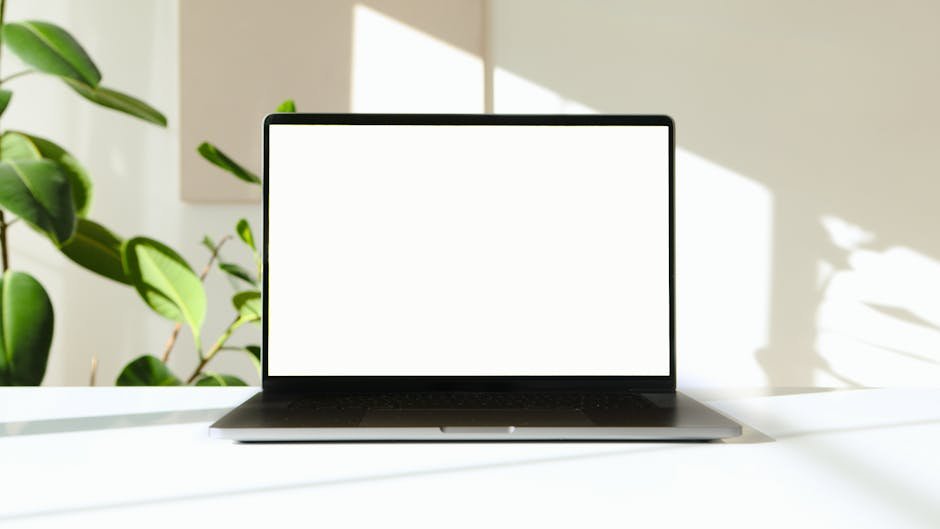 A sleek laptop with a white screen on a desk with green plants in the background.