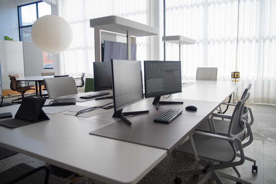 Spacious modern office featuring multiple computers, chairs, and collaborative workstations in natural light.