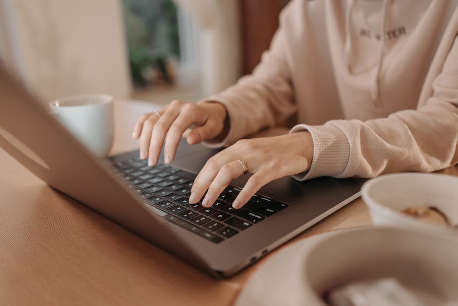 Close-up of a woman typing on a laptop at home, emphasizing remote work and technology.